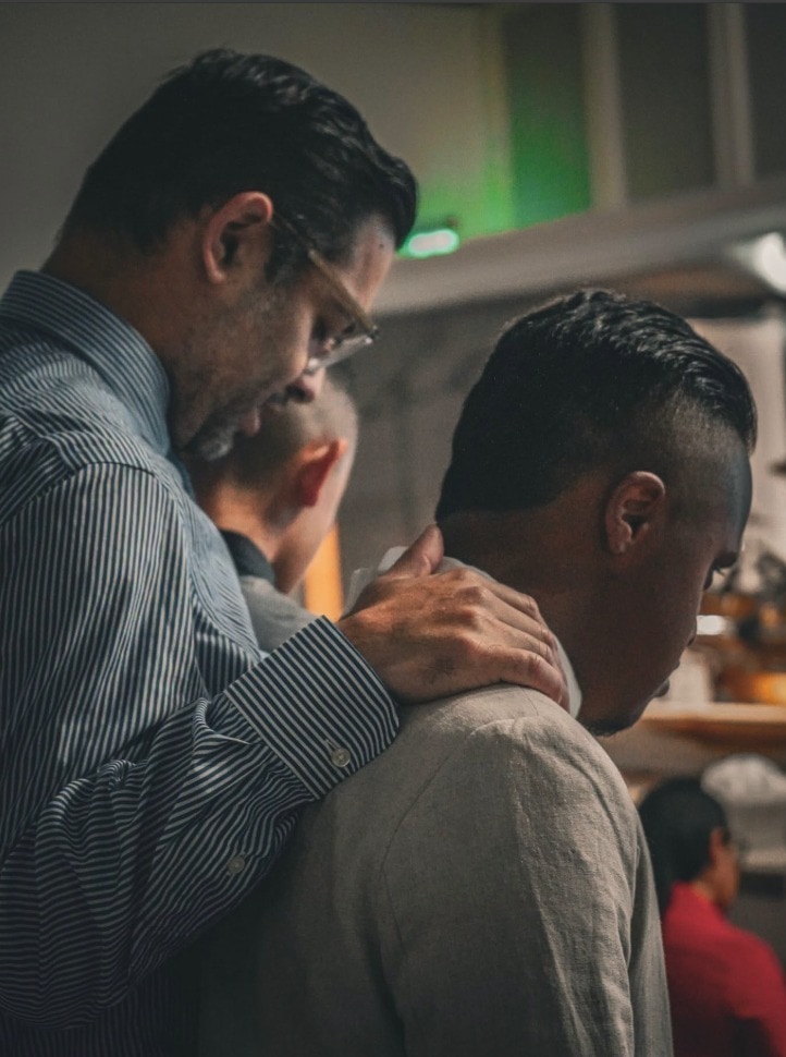 El pastor Samuel Guevara con la mano sobre el hombro de un hombre, orando por él