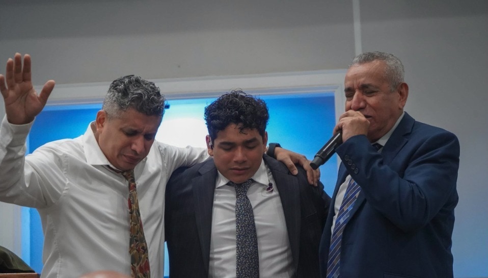 El pastor Samuel Guevara, con la mano levantada, orando con su hijo y el obispo Guevara en la plataforma