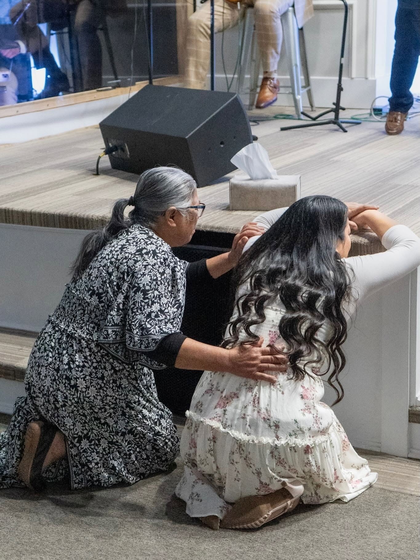 Una mujer mayor arrodillada en oración junto a una joven en el altar
